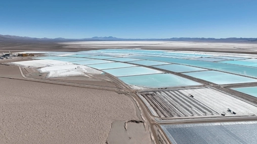 Aerial view of lithium brine evaporation ponds in a desert salt flat with turquoise pools and a clear blue sky