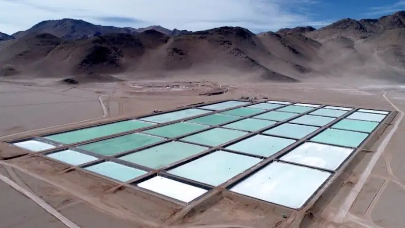 Aerial view of rectangular lithium evaporation ponds in shades of teal and white amid desert mountains