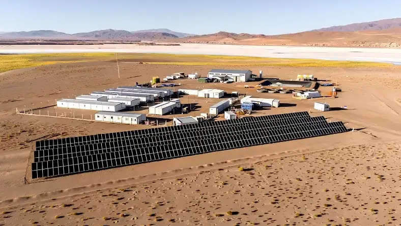 Aerial view of a remote lithium camp in arid desert with solar panels, white buildings, and a salt flat beyond