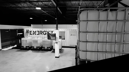 Industrial facility interior with an ENERGYX-branded shipping container and white plastic storage totes